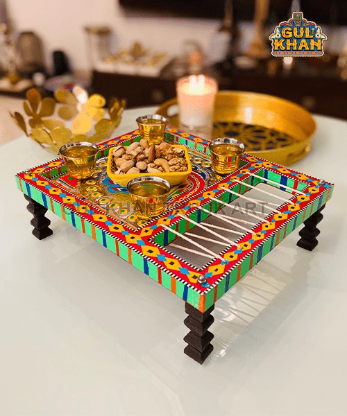 Colorful traditional Indian wooden serving tray with brass cups and a bowl of mixed nuts on a glass table