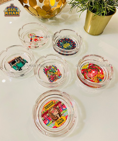 Set of six clear glass ashtrays with colorful Pakistani truck art designs on white table