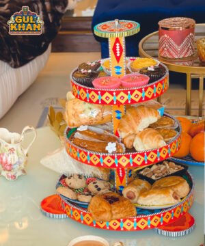 Three-tier colorful cupcake stand with assorted pastries, croissants, cookies on a glass table indoors