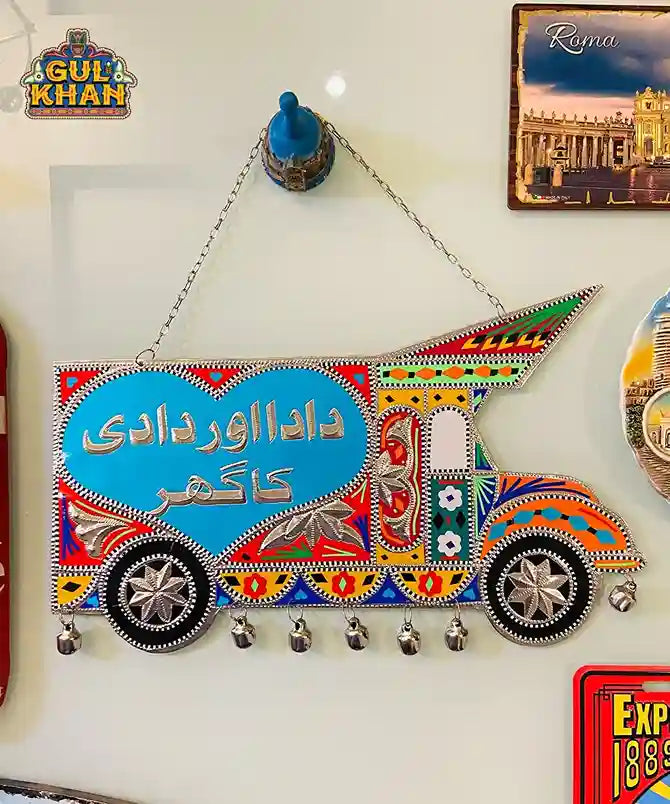 Colorful Pakistani truck art wall hanging with Urdu script and decorative bells on white wall