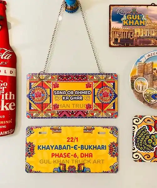 Colorful handcrafted wall plaques with traditional Gul Khan truck art designs and address details hanging on a wall