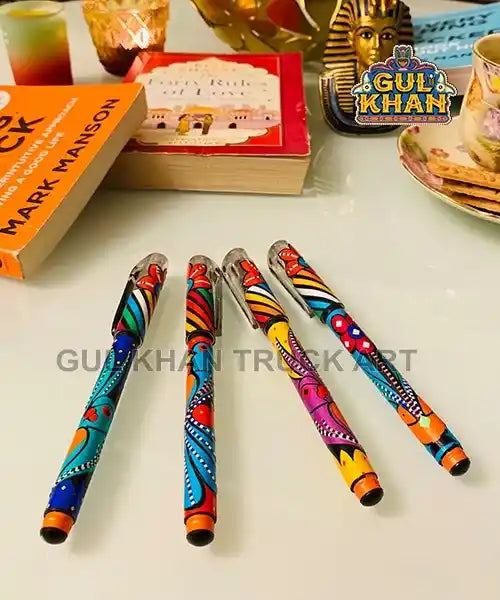 Four colorful hand-painted pens on a table with books, a teacup, and decorative items