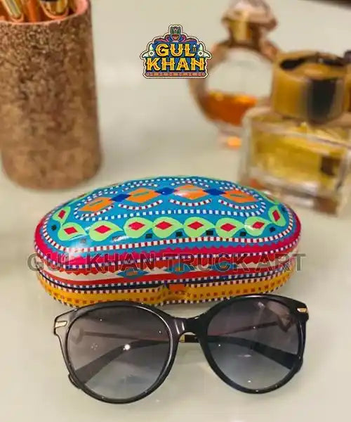 Colorful hand-painted glasses case with blue, red, and green patterns and black sunglasses on a white surface