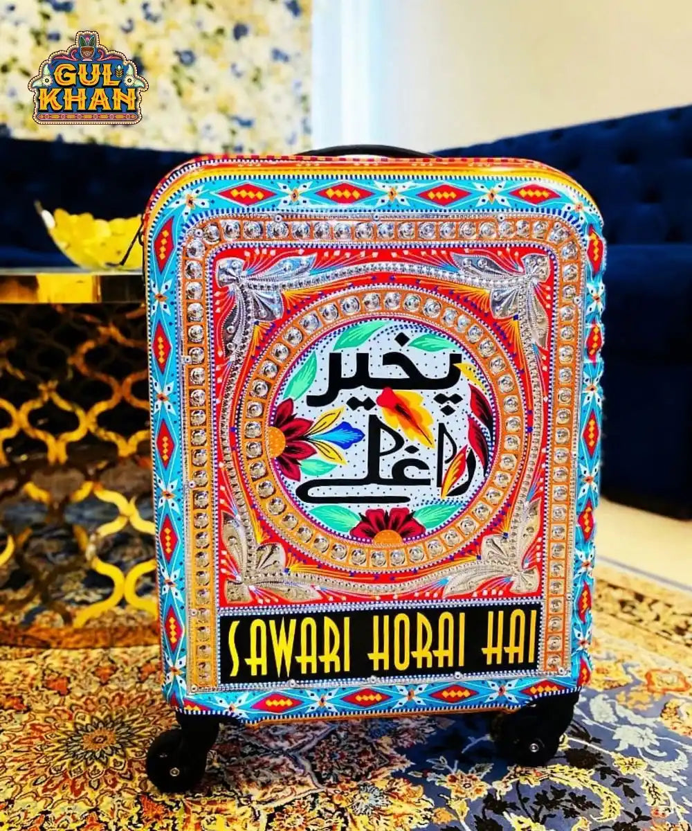 Colorful Gul Khan designer suitcase with hand-painted floral patterns and Urdu text on Persian rug