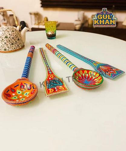 Set of four handpainted wooden spoons with bright ethnic designs on a white table next to a floral teapot
