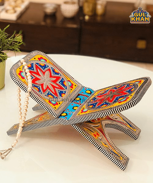 Hand-painted wooden Quran stand with colorful floral patterns and prayer beads on white surface