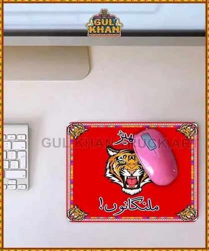 Red mousepad with roaring tiger illustration and Urdu text, pink computer mouse on a gray desk near white keyboard