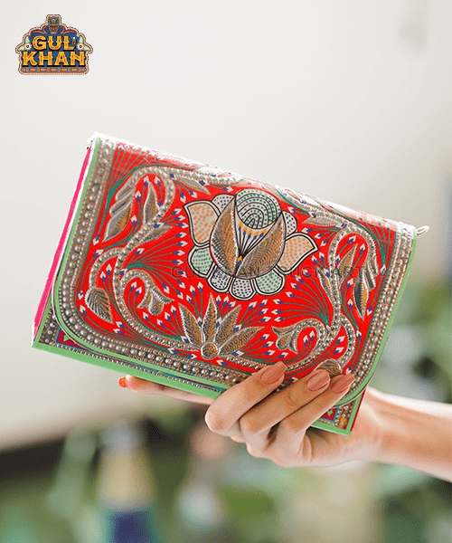 Hand holding a vibrant red and green traditional embroidered clutch bag with floral and paisley patterns