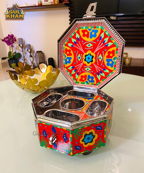Colorful octagonal metal snack box with traditional truck art patterns and multiple compartments open on glass table